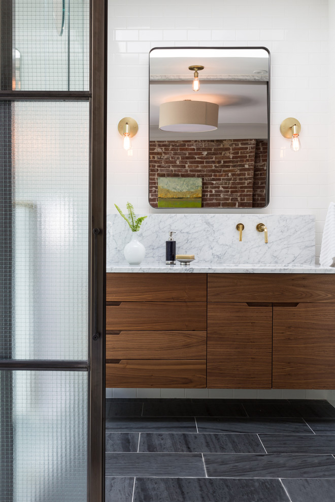 Modern inredning av ett en-suite badrum, med släta luckor, skåp i mellenmörkt trä, en dusch i en alkov, vit kakel, keramikplattor, vita väggar, skiffergolv, ett undermonterad handfat, marmorbänkskiva, grått golv och dusch med gångjärnsdörr