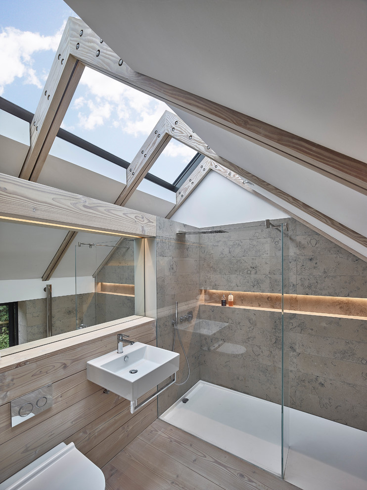 Inspiration for a contemporary bathroom in Manchester with a wall-mounted sink, a built-in shower, a wall mounted toilet, grey tiles, stone tiles and medium hardwood flooring.