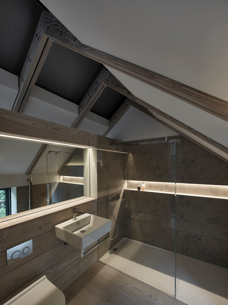 Idéer för funkis badrum, med ett väggmonterat handfat, en kantlös dusch, en vägghängd toalettstol, grå kakel, stenkakel, grå väggar och ljust trägolv