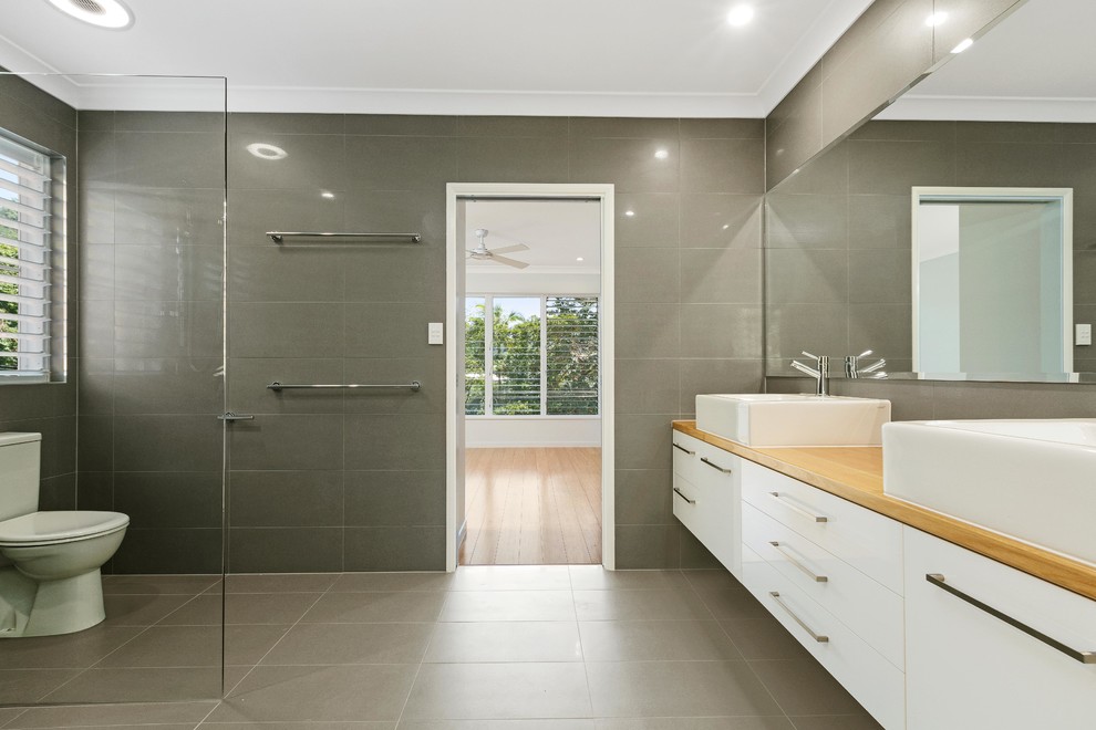 Idée de décoration pour une grande salle de bain minimaliste en bois clair pour enfant avec un placard avec porte à panneau surélevé, un plan de toilette en bois et un carrelage gris.