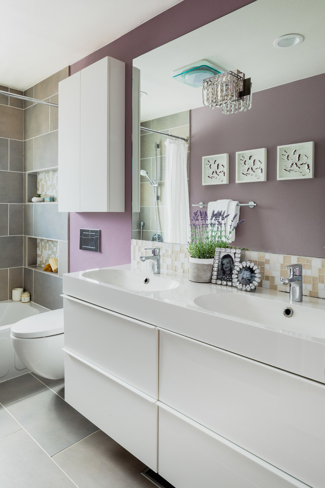 Inspiration for a small contemporary grey and purple family bathroom in Denver with flat-panel cabinets, white cabinets, an alcove bath, a shower/bath combination, a wall mounted toilet, glass tiles, purple walls, ceramic flooring, an integrated sink, solid surface worktops, grey floors, a shower curtain and white worktops.