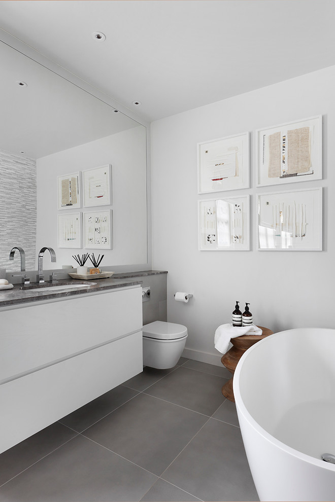 Идея дизайна: серо-белая ванная комната в современном стиле с плоскими фасадами, белыми фасадами, отдельно стоящей ванной, белыми стенами, консольной раковиной и инсталляцией