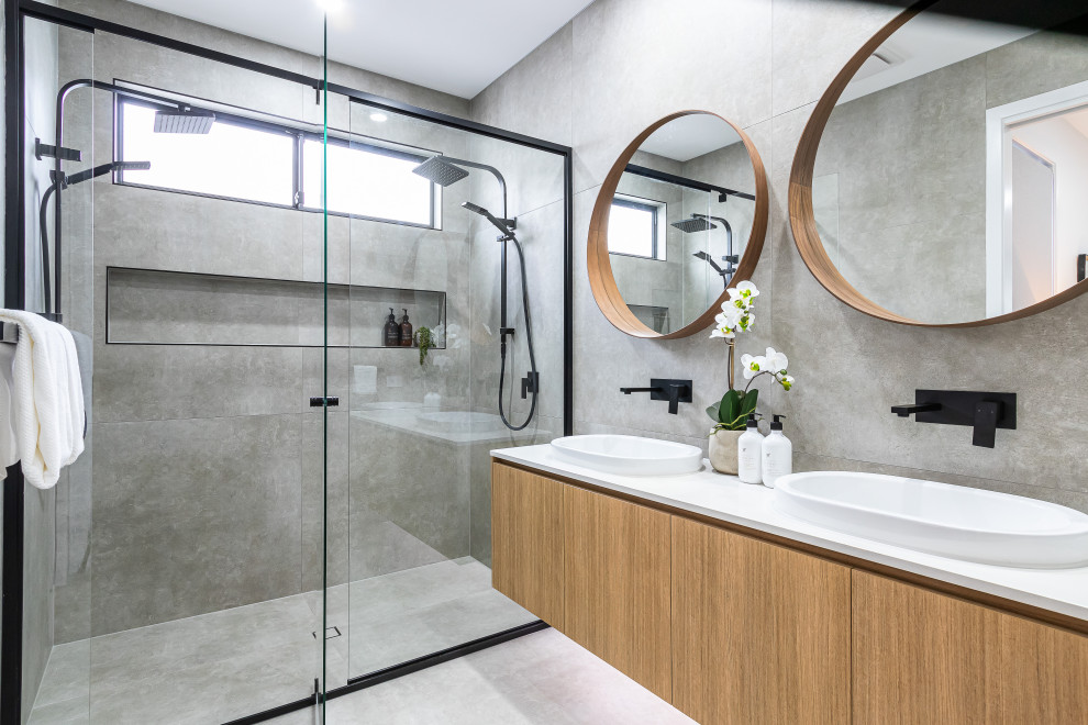 Aménagement d'une grande salle de bain contemporaine en bois brun avec un carrelage gris, une vasque, un sol gris, une cabine de douche à porte battante, un plan de toilette blanc, une niche, meuble double vasque et meuble-lavabo encastré.