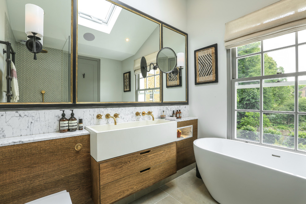 Design ideas for a contemporary bathroom in London with flat-panel cabinets, medium wood cabinets, a freestanding bath, white walls, a trough sink, grey floors and white worktops.