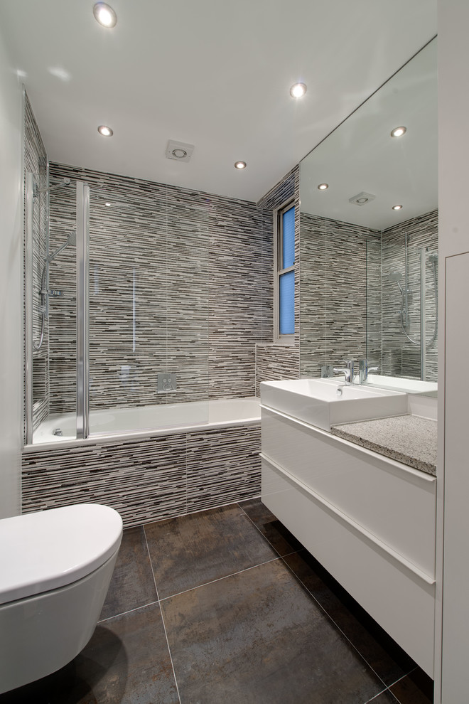 Inredning av ett modernt mellanstort en-suite badrum, med släta luckor, vita skåp, ett platsbyggt badkar, en vägghängd toalettstol, flerfärgad kakel, keramikplattor, vita väggar, klinkergolv i keramik, ett integrerad handfat och granitbänkskiva