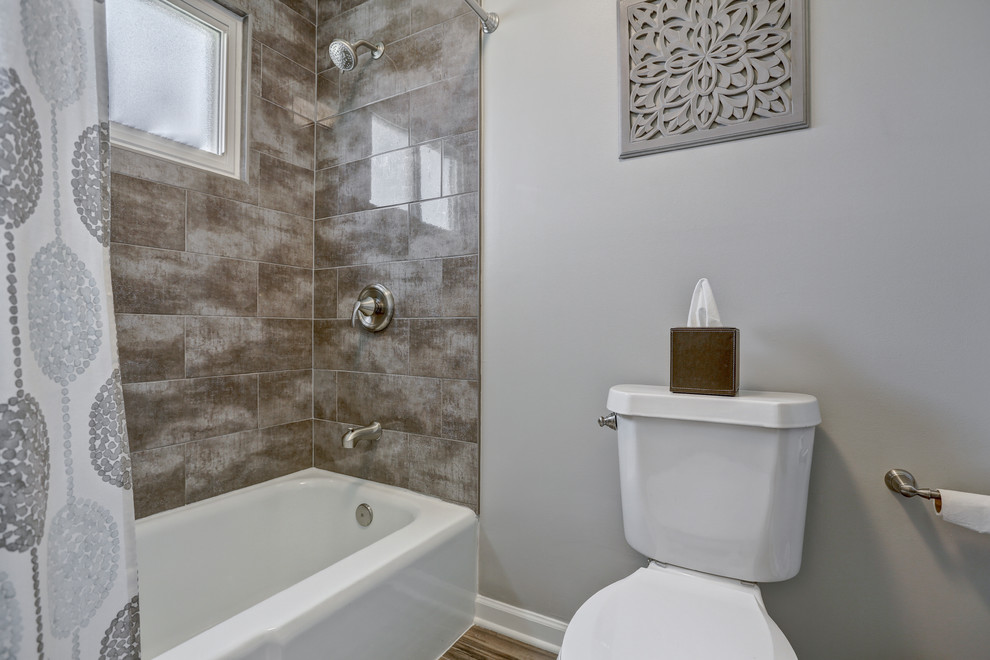 Cette image montre une salle de bain principale traditionnelle de taille moyenne avec un placard à porte shaker, WC séparés, un mur gris, un lavabo encastré, un sol marron, des portes de placard marrons, une baignoire en alcôve, un combiné douche/baignoire, un carrelage marron, des carreaux de céramique, un sol en vinyl, un plan de toilette en marbre et une cabine de douche avec un rideau.