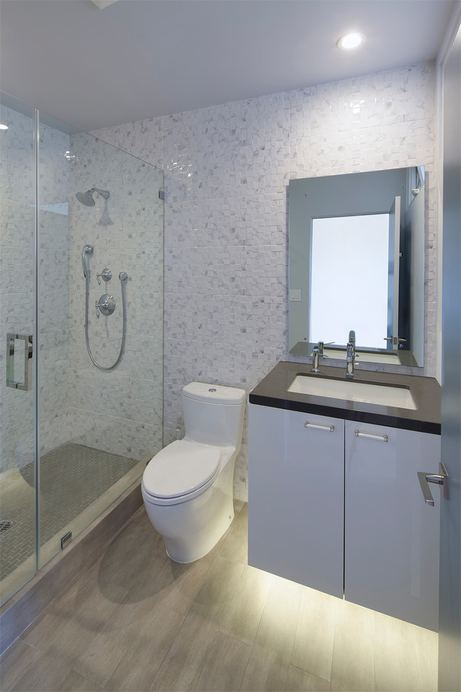 Idée de décoration pour une salle de bain design avec un lavabo encastré, un placard à porte plane, des portes de placard grises, un plan de toilette en calcaire, un carrelage gris, un mur gris et parquet clair.