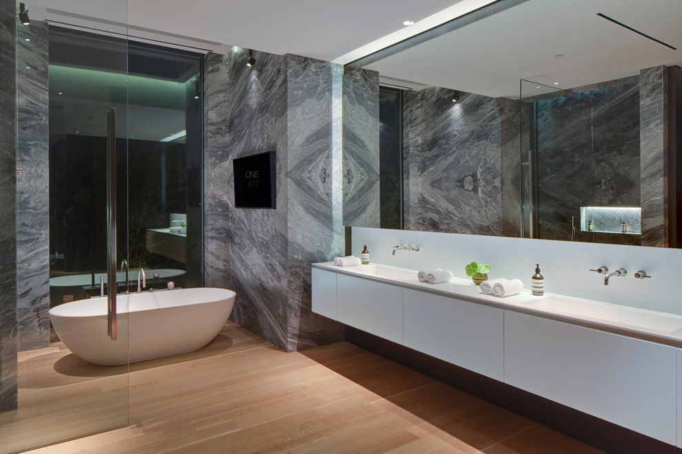 Ejemplo de cuarto de baño actual con lavabo integrado, armarios con paneles lisos, puertas de armario blancas, bañera exenta, paredes blancas y suelo de madera oscura