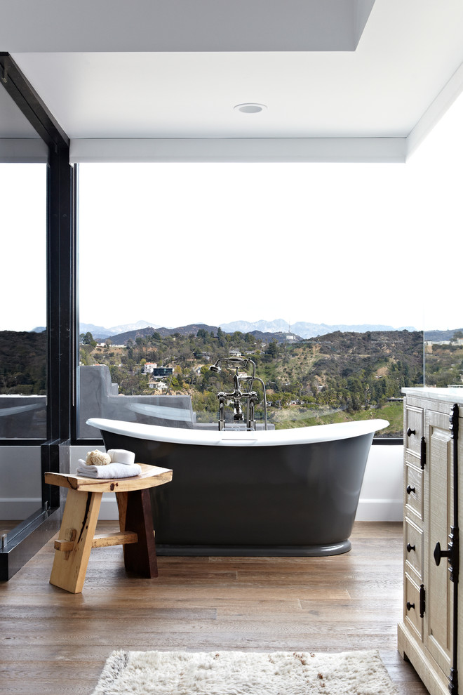 Diseño de cuarto de baño clásico con bañera exenta, armarios con paneles con relieve y suelo de madera oscura
