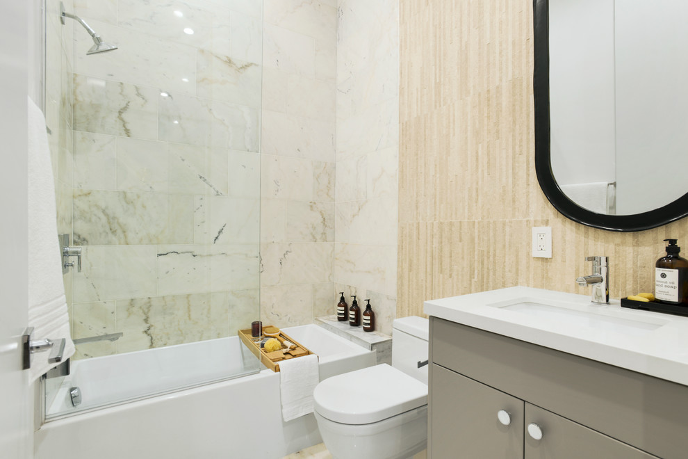 Exemple d'une petite salle de bain tendance avec un placard à porte plane, des portes de placard grises, une baignoire posée, un combiné douche/baignoire, WC à poser, du carrelage en marbre, un sol en marbre, une cabine de douche à porte battante et un plan de toilette blanc.