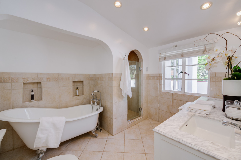 This is an example of a large mediterranean ensuite bathroom in Los Angeles with white cabinets, a claw-foot bath, an alcove shower, a two-piece toilet, a submerged sink, marble worktops and a hinged door.