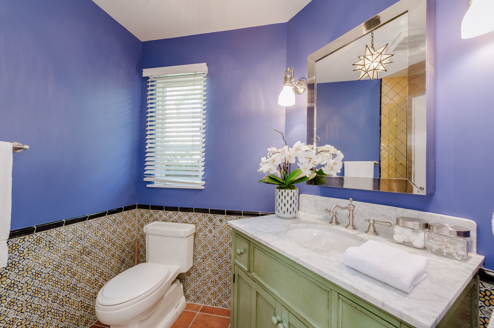 Inredning av ett medelhavsstil litet badrum med dusch, med skåp i shakerstil, gröna skåp, en hörndusch, en toalettstol med separat cisternkåpa, flerfärgad kakel, ett undermonterad handfat, marmorbänkskiva, dusch med gångjärnsdörr, blå väggar, klinkergolv i terrakotta och rött golv