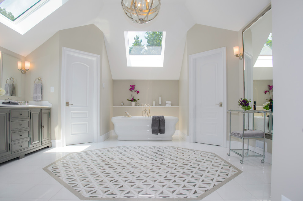 На фото: главная ванная комната в классическом стиле с фасадами с выступающей филенкой, серыми фасадами, отдельно стоящей ванной, бежевой плиткой, каменной плиткой и бежевыми стенами с