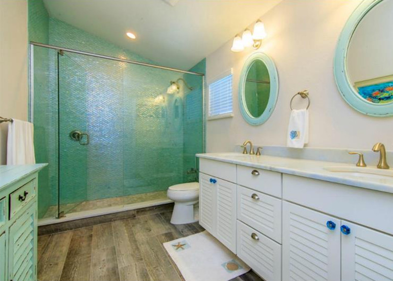 Example of a mid-sized beach style 3/4 blue tile and mosaic tile medium tone wood floor and brown floor alcove shower design in Tampa with louvered cabinets, white cabinets, a two-piece toilet, white walls, an undermount sink, marble countertops and a hinged shower door