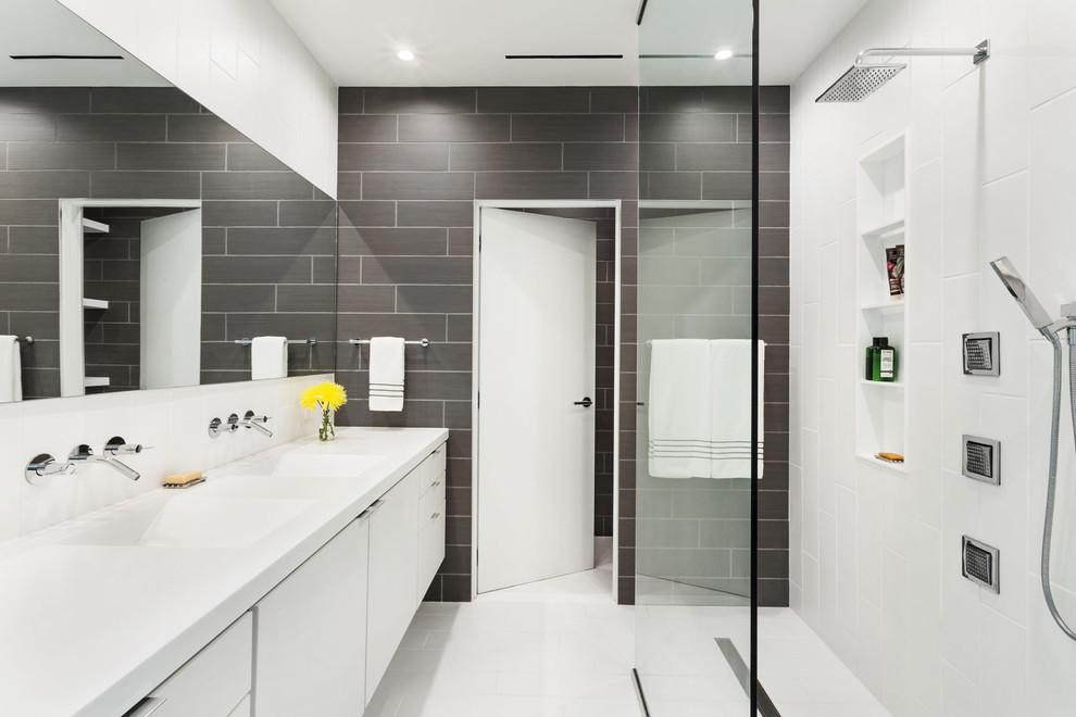 Modern inredning av ett vit vitt badrum, med grå väggar, släta luckor, vita skåp, en öppen dusch, grå kakel, ett integrerad handfat, vitt golv och med dusch som är öppen