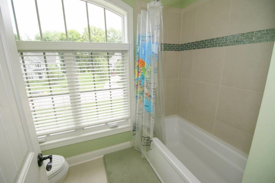 Cette image montre une salle de bain traditionnelle de taille moyenne pour enfant avec une baignoire posée, un combiné douche/baignoire, WC à poser, un carrelage beige, des carreaux de porcelaine, un mur vert et un sol en carrelage de porcelaine.