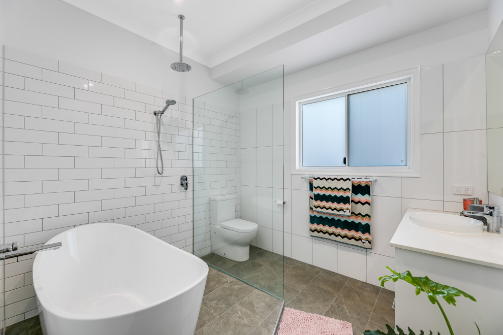 Bild på ett funkis vit vitt badrum, med vita skåp, ett fristående badkar, våtrum, vit kakel, vita väggar, ett nedsänkt handfat, grått golv och med dusch som är öppen
