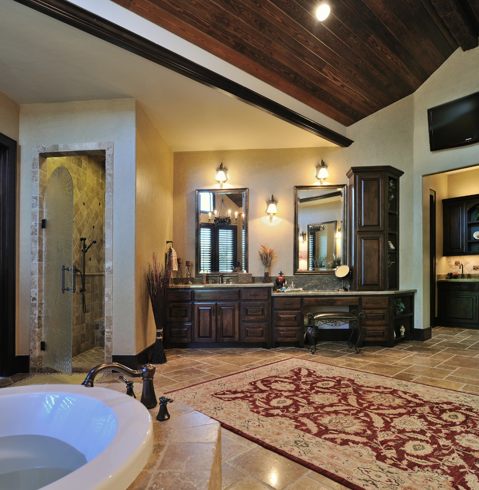 Inspiration for a large timeless master brown tile and stone tile travertine floor bathroom remodel in Houston with raised-panel cabinets, dark wood cabinets, granite countertops, a one-piece toilet, a drop-in sink and beige walls