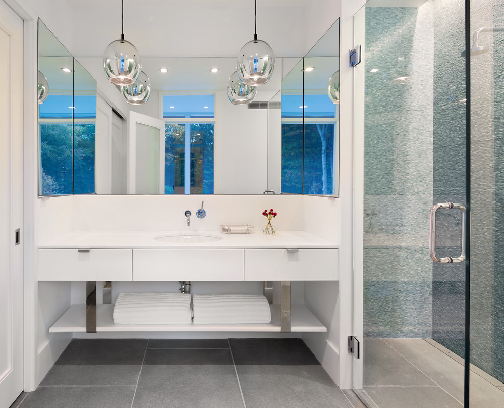 Modernes Badezimmer mit flächenbündigen Schrankfronten, weißen Schränken, bodengleicher Dusche, blauen Fliesen, Porzellanfliesen, Porzellan-Bodenfliesen, Unterbauwaschbecken, Mineralwerkstoff-Waschtisch, weißer Wandfarbe und Falttür-Duschabtrennung in New York