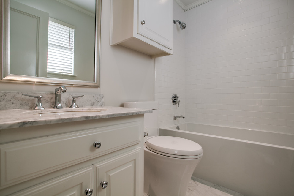 Bild på ett litet vintage badrum med dusch, med luckor med upphöjd panel, vita skåp, ett badkar i en alkov, en dusch/badkar-kombination, en toalettstol med hel cisternkåpa, vit kakel, tunnelbanekakel, grå väggar, marmorgolv, ett undermonterad handfat, marmorbänkskiva, vitt golv och dusch med duschdraperi