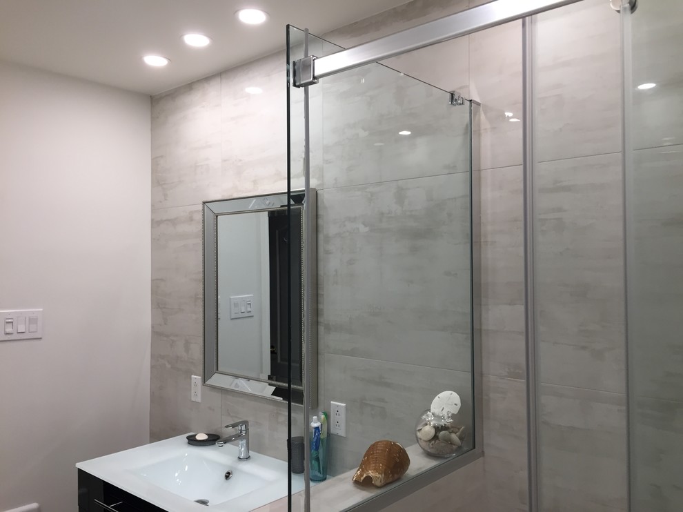Idéer för mellanstora funkis en-suite badrum, med släta luckor, svarta skåp, en hörndusch, grå kakel, porslinskakel, grå väggar, klinkergolv i porslin, ett integrerad handfat, bänkskiva i glas, grått golv och dusch med skjutdörr