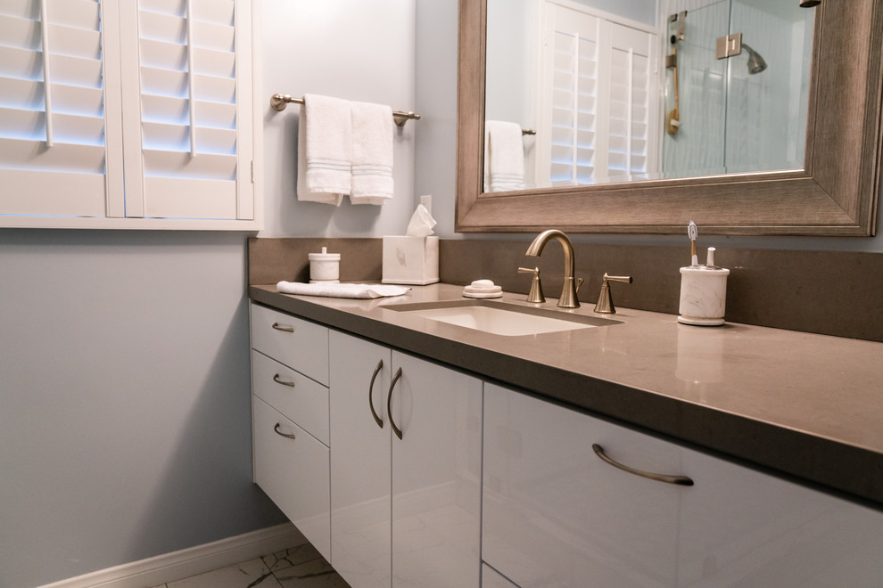 This is an example of a medium sized eclectic ensuite bathroom in Los Angeles with recessed-panel cabinets, white cabinets, a corner shower, a one-piece toilet, grey walls, pebble tile flooring, a built-in sink, quartz worktops and grey worktops.