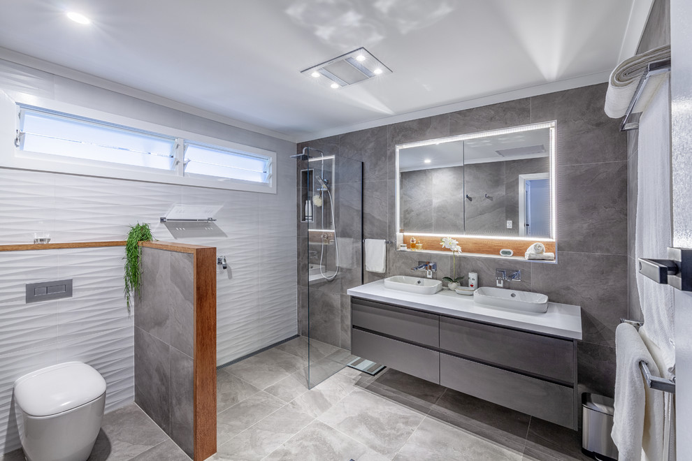 Modernes Duschbad mit flächenbündigen Schrankfronten, grauen Schränken, Nasszelle, Toilette mit Aufsatzspülkasten, grauen Fliesen, weißen Fliesen, Aufsatzwaschbecken, grauem Boden, offener Dusche und weißer Waschtischplatte in Brisbane