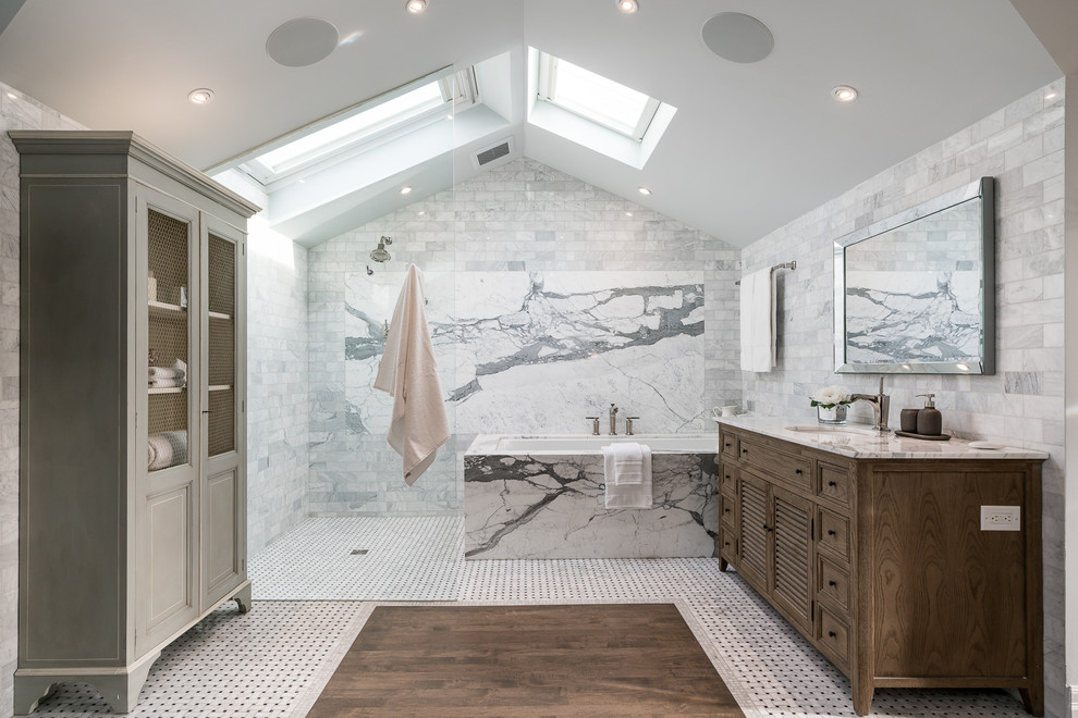 Inredning av ett klassiskt vit vitt badrum, med skåp i mellenmörkt trä, ett undermonterat badkar, en kantlös dusch, grå kakel, vit kakel, tunnelbanekakel, vita väggar, mosaikgolv, ett undermonterad handfat, vitt golv, med dusch som är öppen och luckor med infälld panel