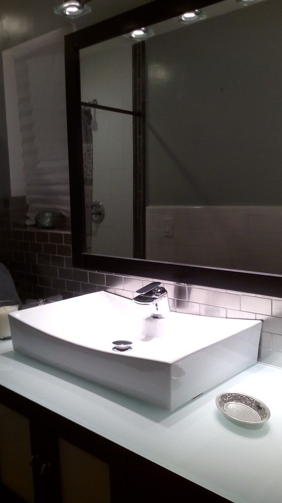 Exemple d'une petite salle de bain principale moderne avec une vasque, un placard en trompe-l'oeil, des portes de placard noires, un plan de toilette en verre, une douche ouverte, un carrelage gris, carrelage en métal, un mur gris et un sol en bois brun.