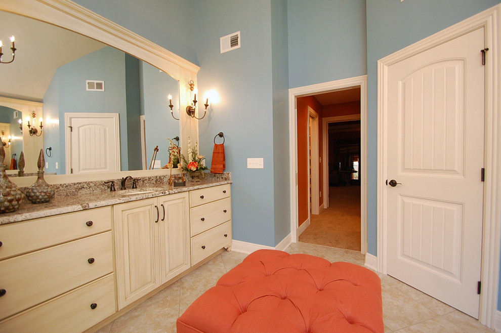 Bild på ett mellanstort vintage en-suite badrum, med släta luckor, skåp i slitet trä, en toalettstol med separat cisternkåpa, blå väggar, kalkstensgolv, ett undermonterad handfat och granitbänkskiva