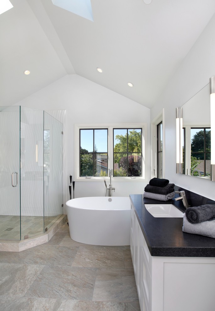 Bild på ett vintage badrum, med ett undermonterad handfat, vita skåp, ett fristående badkar, en dusch i en alkov, grå kakel och vita väggar