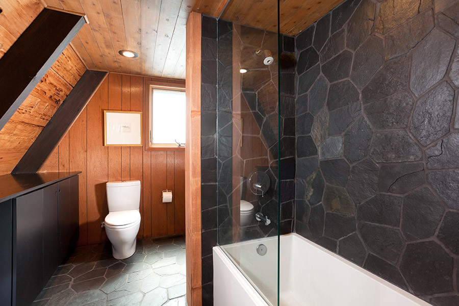 Aménagement d'une salle de bain principale rétro de taille moyenne avec des portes de placard noires, un combiné douche/baignoire, WC à poser, un carrelage noir, un mur marron, un sol en ardoise, un placard à porte plane et une baignoire en alcôve.