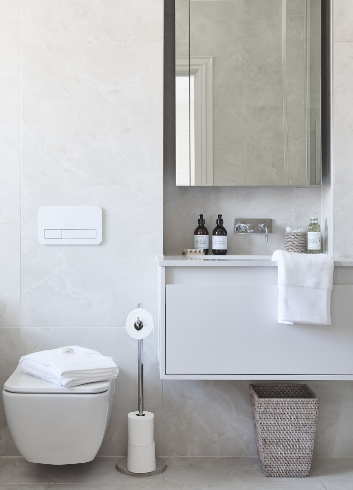 Cette image montre une salle de bain design avec un placard à porte plane, des portes de placard blanches, un mur blanc, un sol gris et un plan de toilette blanc.