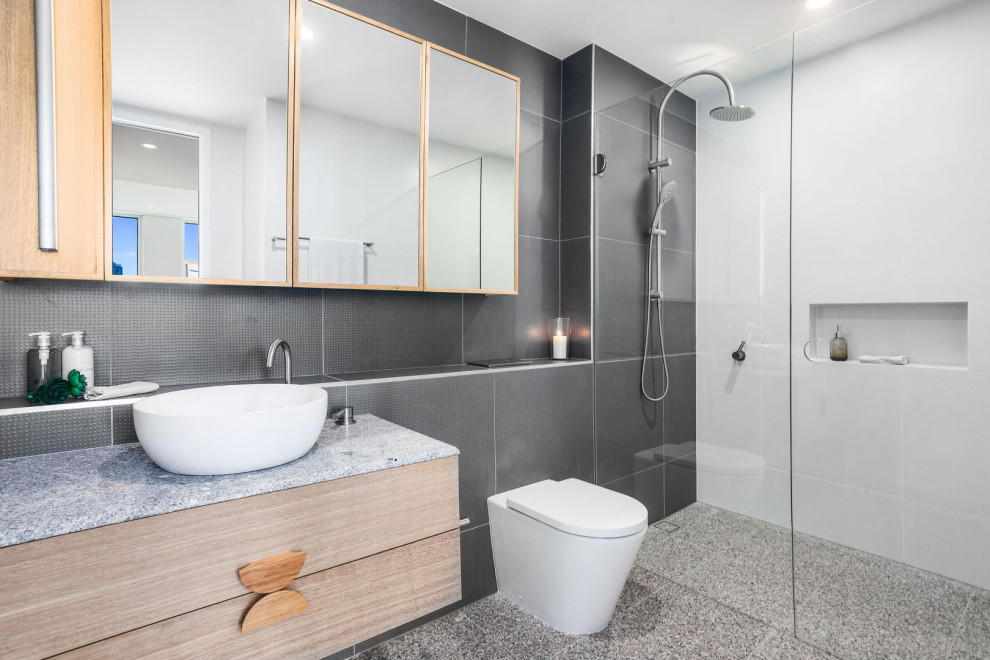 Inredning av ett modernt grå grått badrum med dusch, med släta luckor, skåp i mellenmörkt trä, en dusch i en alkov, en toalettstol med hel cisternkåpa, grå kakel, vita väggar, ett fristående handfat, grått golv och med dusch som är öppen