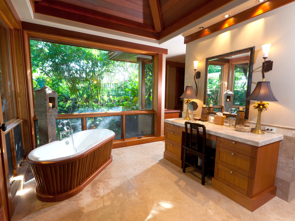 Exotisk inredning av ett en-suite badrum, med möbel-liknande, skåp i mellenmörkt trä, ett fristående badkar, beige kakel och stenhäll