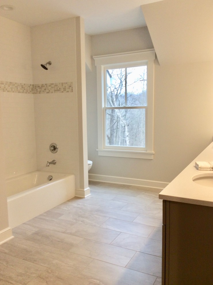 This is an example of a large farmhouse family bathroom in Columbus with flat-panel cabinets, grey cabinets, a built-in bath, a shower/bath combination, a one-piece toilet, white tiles, metro tiles, grey walls, ceramic flooring, a submerged sink and engineered stone worktops.