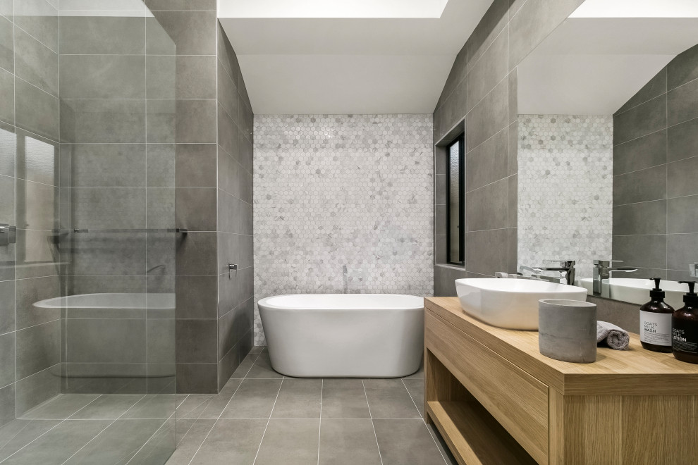 This is an example of a contemporary ensuite bathroom in Melbourne with open cabinets, light wood cabinets, a freestanding bath, a walk-in shower, grey tiles, wooden worktops, grey floors, an open shower, a single sink and a freestanding vanity unit.