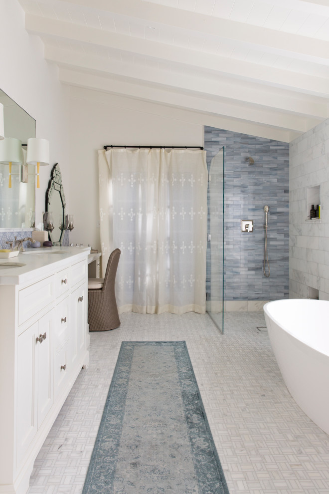 Пример оригинального дизайна: главная ванная комната в средиземноморском стиле с белыми фасадами, душем без бортиков, синей плиткой, белыми стенами, белым полом, белой столешницей, встроенной тумбой, сводчатым потолком, фасадами с утопленной филенкой, удлиненной плиткой, полом из керамогранита, тумбой под две раковины, отдельно стоящей ванной, врезной раковиной и открытым душем