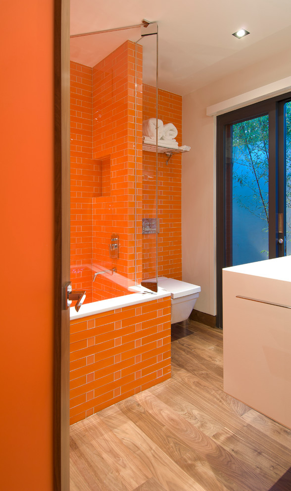 На фото: детская ванная комната среднего размера в стиле модернизм с белыми фасадами, ванной в нише, душем над ванной, унитазом-моноблоком, оранжевой плиткой, оранжевыми стенами, светлым паркетным полом, бежевым полом, душем с распашными дверями, белой столешницей, подвесной тумбой и многоуровневым потолком