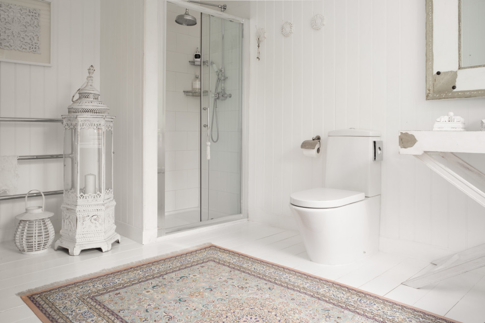 Shabby chic-inspirerad inredning av ett vit vitt badrum, med vita skåp, en dusch i en alkov, en toalettstol med separat cisternkåpa, vit kakel, vita väggar, målat trägolv, vitt golv och dusch med skjutdörr