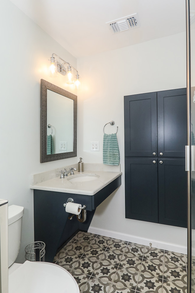Example of a mid-sized transitional 3/4 white tile and porcelain tile porcelain tile and multicolored floor bathroom design in Atlanta with recessed-panel cabinets, blue cabinets, a two-piece toilet, gray walls, an undermount sink, quartz countertops, a hinged shower door and white countertops