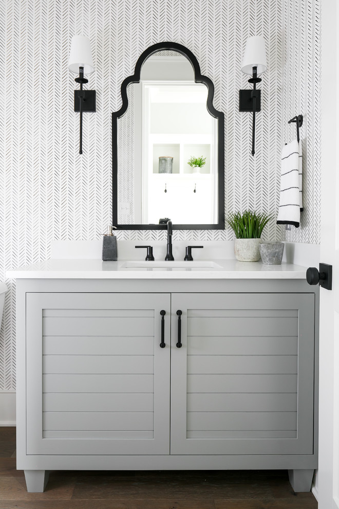 На фото: ванная комната в стиле неоклассика (современная классика) с серыми фасадами, разноцветными стенами, темным паркетным полом, врезной раковиной, коричневым полом, белой столешницей, зеркалом с подсветкой и фасадами в стиле шейкер с