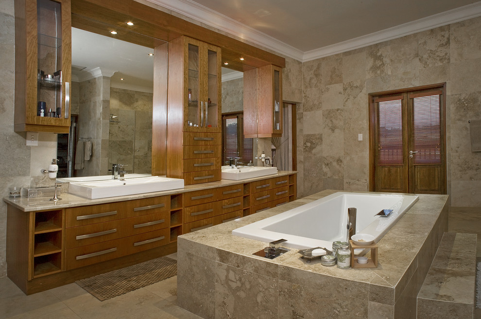 Klassisches Badezimmer mit Aufsatzwaschbecken, flächenbündigen Schrankfronten, hellbraunen Holzschränken, Einbaubadewanne und Travertinfliesen in Sonstige