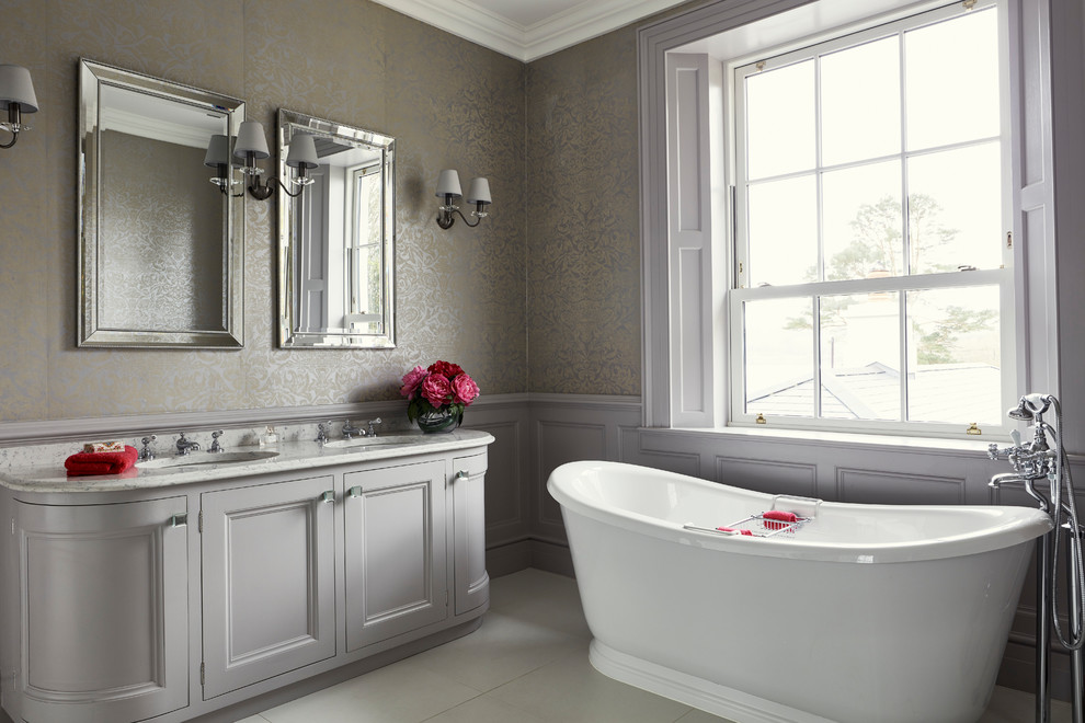 На фото: ванная комната среднего размера в стиле неоклассика (современная классика) с фасадами с утопленной филенкой, серыми фасадами, отдельно стоящей ванной, душем над ванной, серыми стенами и серым полом с