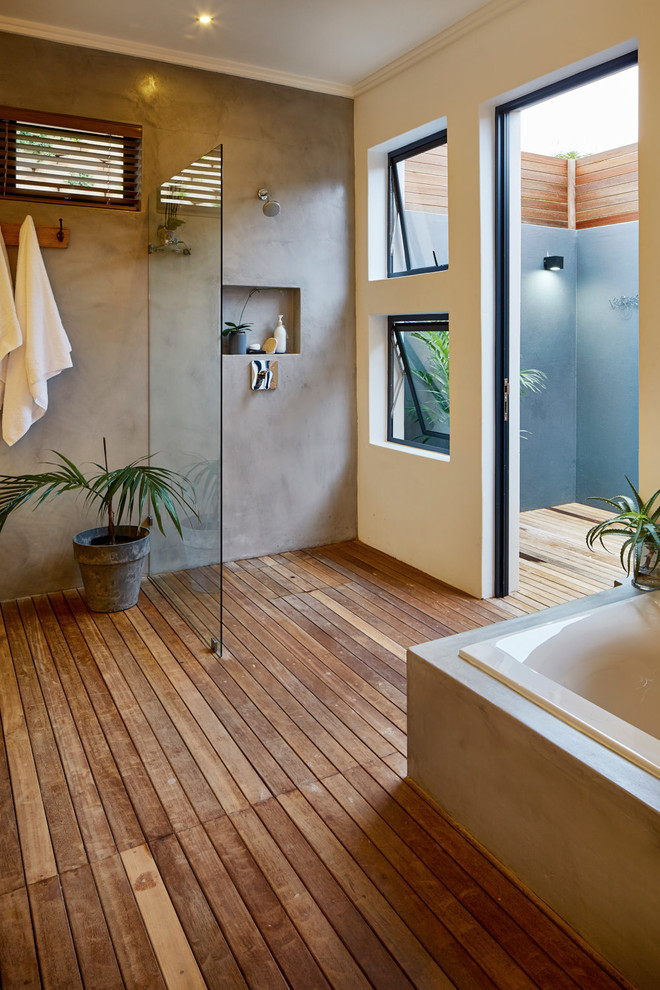 Réalisation d'une salle de bain marine avec une baignoire posée, une douche ouverte, un mur gris, un sol en bois brun et aucune cabine.