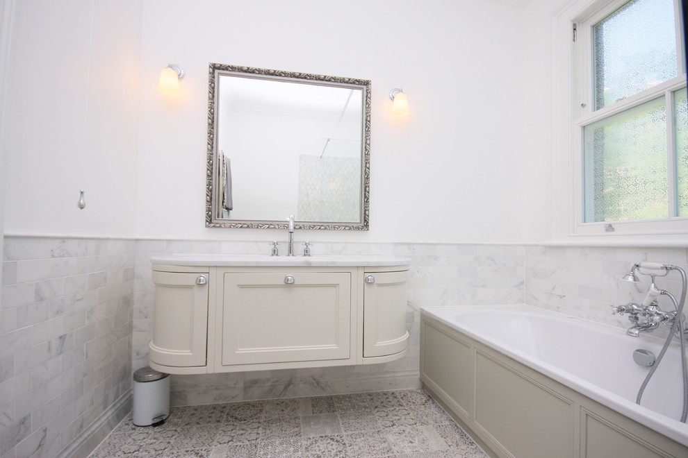 Стильный дизайн: большая главная ванная комната в викторианском стиле с фасадами в стиле шейкер, бежевыми фасадами, угловой ванной, душевой комнатой, инсталляцией, серой плиткой, керамогранитной плиткой, белыми стенами, полом из керамогранита, накладной раковиной, мраморной столешницей, серым полом, открытым душем и белой столешницей - последний тренд