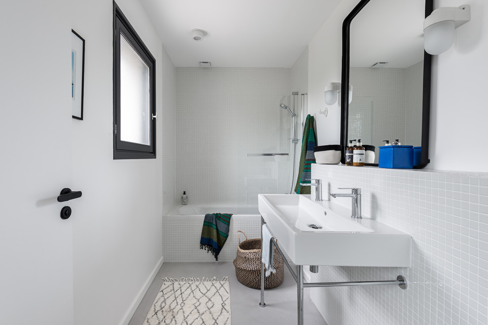 Exemple d'une petite salle de bain bord de mer pour enfant avec une baignoire posée, un combiné douche/baignoire, un carrelage blanc, mosaïque, un mur blanc, sol en béton ciré, un plan vasque, un sol gris, une cabine de douche à porte battante et WC suspendus.