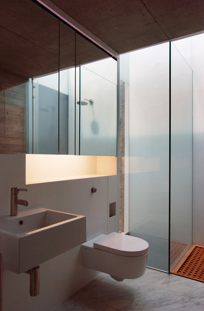 Ejemplo de cuarto de baño actual de tamaño medio con aseo y ducha, encimera de acrílico, sanitario de pared, ducha empotrada, lavabo suspendido, paredes blancas y suelo de mármol