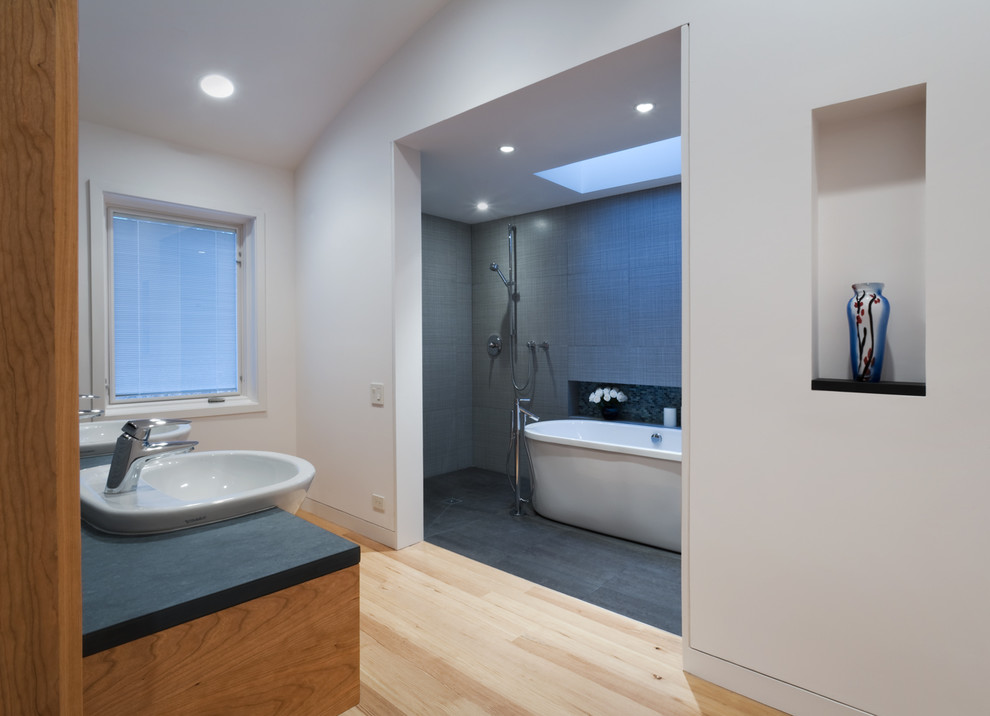 Cette image montre une salle de bain principale minimaliste en bois brun de taille moyenne avec un lavabo posé, un placard à porte plane, une baignoire indépendante, une douche ouverte, WC à poser, un carrelage gris, des carreaux de porcelaine, un mur blanc et un sol en carrelage de porcelaine.