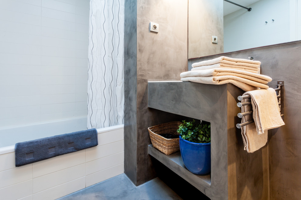 Photo of a medium sized mediterranean ensuite bathroom in Barcelona with an integrated sink, open cabinets, grey cabinets, concrete worktops, a shower/bath combination, a two-piece toilet, white tiles, white walls and concrete flooring.